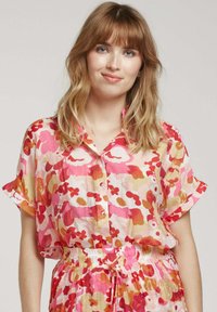 Chemise à motifs floraux en rose, orange et crème. Tissu léger avec des manches courtes, fermeture à boutons sur le devant et coupe décontractée. Taille élastique.