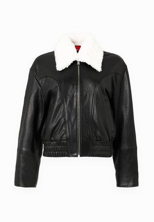 Veste en cuir noire coupée avec un col en fausse fourrure blanche, dotée d'une fermeture éclair à l'avant, d'un ourlet élastiqué et de coutures cintrées pour la structure.