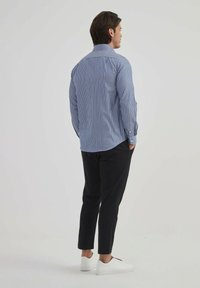 Chemise rayée bleue avec un col classique, des manches longues et une coupe décontractée, associée à un pantalon noir et des baskets blanches.