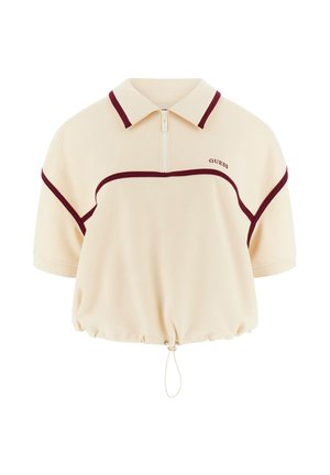 Polo corta beige con rifiniture color marrone scuro, maniche corte, cerniera frontale, orlo con coulisse e logo "GUESS" sul petto.