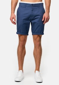 Shorts bleu marine en tissu texturé, avec ourlets retroussés, fermeture à bouton et poches, assortis à des baskets blanches.