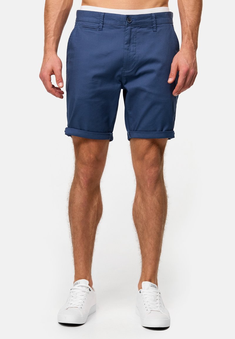 Shorts bleu marine en tissu texturé, avec ourlets retroussés, fermeture à bouton et poches, assortis à des baskets blanches.