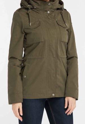 Femme portant une veste à capuche vert olive avec poches frontales, boutons métalliques et fermeture éclair, associée à un jean bleu foncé.