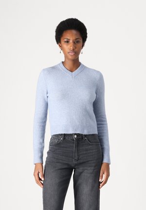 Lys blå cropped genser med V-hals, ribbede mansjetter og kant, laget av mykt materiale. Kombinert med høyt midjede mørke jeans.
