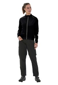 Svart zip-up jacka med en texturerad övre del, reflekterande accenter och långa ärmar. Tillsammans med mörka cargobyxor och cykelskor.