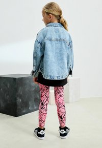 Jeansjacka, ljusblå, oversized passform, ihopparad med rosa leggings som har svarta abstrakta mönster. Svarta sneakers med vita detaljer.