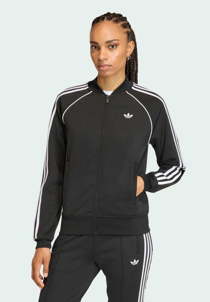 Giacca sportiva nera con strisce bianche lungo le maniche, zip frontale, polsini a coste e un piccolo logo sul petto.