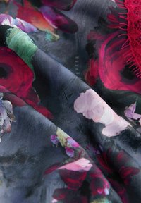 Tessuto con motivo floreale che presenta rose rosse e rosa vivaci su uno sfondo scuro, realizzato in un materiale liscio e leggermente trasparente con un bordo testurizzato.