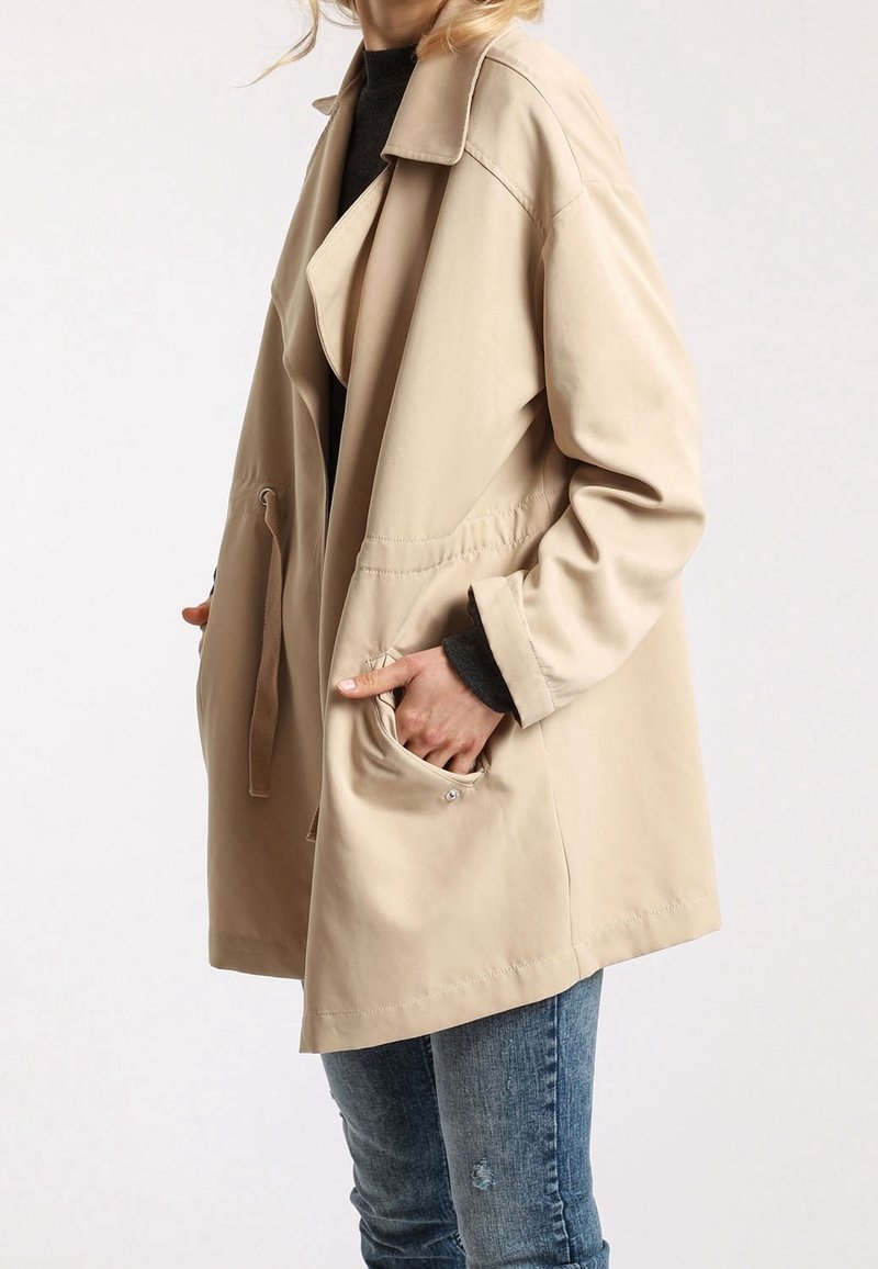 Chaqueta de abrigo beige con un ajuste relajado, cuello grande, cintura ceñida y dos bolsillos delanteros. Fabricada en un tejido ligero y suave, con mangas largas.