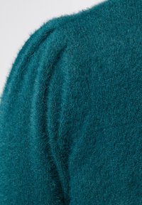 Teal trui met een zachte, pluizige textuur en geplooide details op de schouder. De stof lijkt licht en warm te zijn.