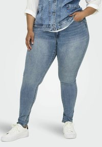 Jeans ajustados de color azul claro hechos de denim, con una cintura de altura media, bolsillos frontales y un acabado liso. Combinados con zapatillas blancas.