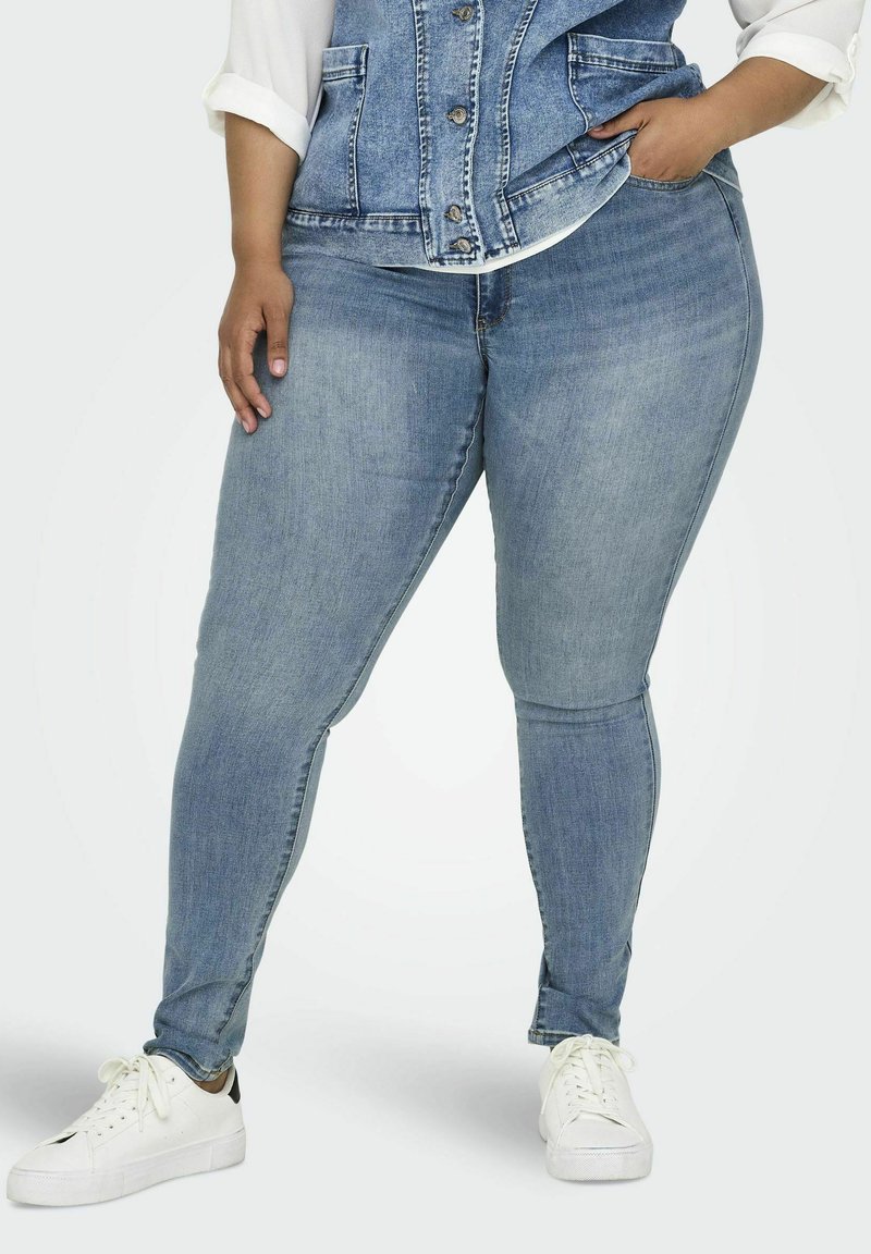 Jeans ajustados de color azul claro hechos de denim, con una cintura de altura media, bolsillos frontales y un acabado liso. Combinados con zapatillas blancas.
