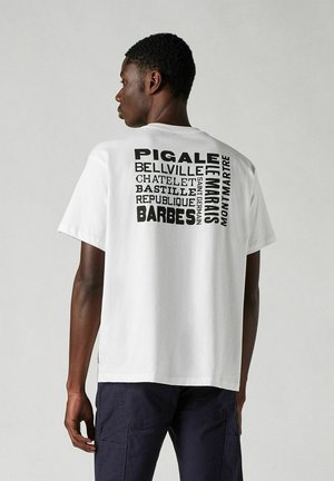 Weißes Baumwoll-T-Shirt mit fettem schwarzen Text und Städtenamen auf dem Rücken. Lockerer Schnitt mit kurzen Ärmeln und rundem Ausschnitt.