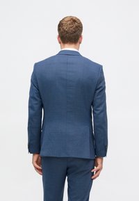 Sacou albastru confecționat dintr-un material texturat, având o deschidere unică în spate, o croială ajustată și mansete cu nasturi.