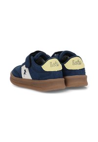 Zapatillas azul marino con una correa de velcro, logo lateral blanco, suela de goma y pestaña en el talón amarilla. Tejido suave con un acabado texturizado.