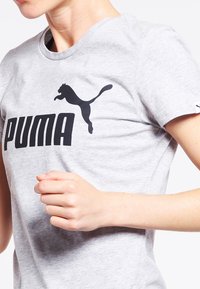 Szara bawełniana koszulka z wyraźnym czarnym logo "PUMA" oraz sylwetką skaczącego pumy. Krótkie rękawy, okrągły dekolt, minimalistyczny design.