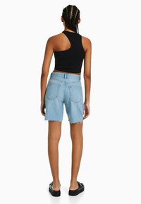 Schwarzes geripptes Cropped-Top mit offenem Rücken, kombiniert mit hellblauen Jeansshorts mit fransigem Saum und zwei Gesäßtaschen. Schwarze Plateausandalen.
