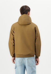 Bruine, hoodie met een relaxte pasvorm, elastische manchetten en tailleband. De achterkant toont een textuurstof en minimale ontwerpelementen.