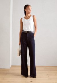 White tank top and navy wide-leg pants with a black belt. Woman holds a light-colored clutch. Smooth textures and minimalistic design.