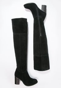 Stivali neri in suede sopra il ginocchio con tacco largo e zip laterale. Il design presenta una texture liscia e cuciture verticali.
