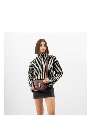 Žena v černobílém roláku se vzorem zebry, černé kožené mini sukni a s burgundskou kabelkou přes rameno.