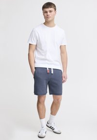 Hvid kortærmet t-shirt parret med navy blå bomulds shorts. Shortsen har elastisk talje og sidelommer. Hvide sokker og sneakers.
