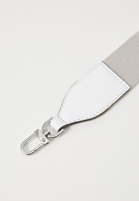Vit läderaxelrem med en texturerad yta, kompletterad av en grå vävd sektion och silverfärgad metalldetalj.