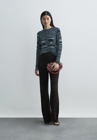 Svarta utsvängda byxor med en texturerad chevronmönster, parat med en marinblå randig stickad tröja. Håller en mönstrad väska med Kedjehandtag.