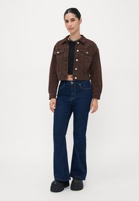 Bruine cropped corduroy jacket met zilveren knopen, zwarte fitted top, donkerblauwe flare jeans en zwarte plateau schoenen. Eenvoudig, modern ontwerp.