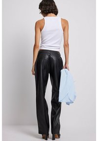 Svarta läderbyxor med hög midja och raka ben, kombinerat med en vit tank top, en ljusblå skjorta draperad över armen och högklackade skor.