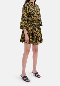 Sukienka krótko rękawowa w żółto-czarny wzór z marszczoną talią, rozkloszowanym dołem i małym kołnierzykiem. Połączona z czarnymi, eleganckimi klapkami na obcasie.
