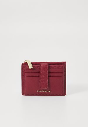 Burgundy leather wallet with textured finish, a top zipper, and multiple card slots; gold logo at the bottom front.