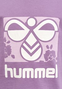 Lilla bomulds T-shirt med et stort hvidt grafisk motiv, der viser et abstrakt design og ordet "hummel" nederst. Teksturen er blød.