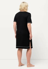 Schwarzes Kurzarmkleid mit geradem Schnitt, versehen mit silbernen Akzenten und seitlichen Schlitzen für zusätzliche Bewegungsfreiheit. Weiche Textur.