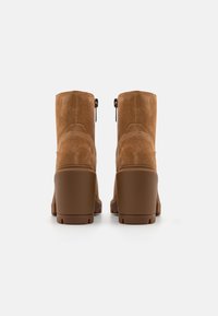 Bottes chelsea en cuir suédé marron, avec une finition texturée, un bout arrondi et un talon épais. Elles comportent des fermetures éclair sur le côté et des détails de couture.
