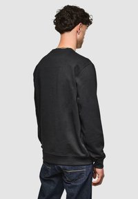 Sudadera negra de manga larga y cuello redondo, con una superficie texturizada y un pequeño detalle de costura en la parte posterior. Combina con denim oscuro.
