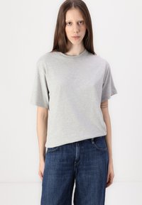 Grå bomulls T-skjorte med korte ermer og rund hals, med diskret logo på brystet, kombinert med mørkeblå jeans.