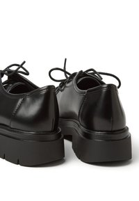 Scarpe di pelle nere con finitura liscia, punta arrotondata e suola piatta in gomma. Presentano lacci e dettagli di cucitura discreti sulla parte superiore.