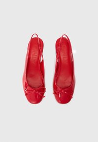 Röda lackläder slingback-lägenheter med rundad tå, knutdetalj fram och en slät yta. Varumärket syns på innersulan.