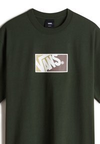 Grön bomulls-t-shirt med rund halsringning. Framsidan har ett rektangulärt Vans-logotyp i beige och brunt. Korta ärmar och avslappnad passform.
