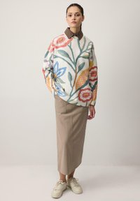 Suéter con un patrón floral en múltiples colores, combinado con una falda midi beige. Zapatillas blancas completan el conjunto.