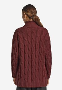 Burgundy kabelstickad tröja med hög krage, långa ärmar och ribbad mudd. Har ett texturerat mönster och en lös passform.