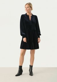 Robe en velours noir à manches longues, col froncé, jupe à volants et coupe décontractée, accompagnée de bottes noires à hauteur de cheville.