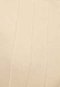 Beige ribbad stickad tyg med vertikala kabelstickningsmönster jämnt fördelade över ytan.