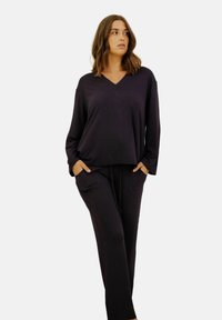 Ensemble de vêtements d'intérieur violet foncé comprenant un haut à col en V à manches longues et un pantalon ample avec poches latérales. Texture douce et lisse.