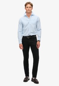 Jasnoniebieska koszula z kołnierzykiem, w zestawieniu z czarnymi dopasowanymi dżinsami i ciemnymi butami. Do wyróżniających się detali należy kieszeń na piersi i pasek.