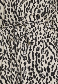 Tissu à imprimé animal beige et noir avec des boutons noirs et une ceinture nouée autour de la taille, montrant les détails et la texture du vêtement.