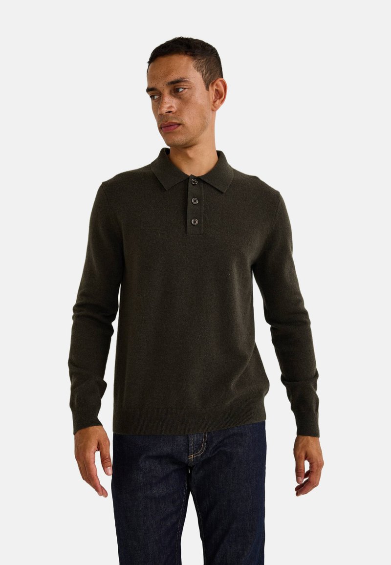 Polo en laine à manches longues de couleur vert foncé avec un col, patte de boutonnage à trois boutons et manches à bord côtelé, associé à un jean foncé.
