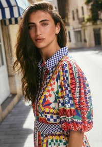 Colorful patterned dress with a blue checkered collar and sleeves. Features bold geometric shapes and vibrant red, green, and yellow accents.