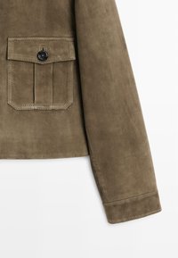 Brauner Wildlederjackenärmel und geknöpftes Klappentasche mit sichtbaren Nähten auf weißem Hintergrund.